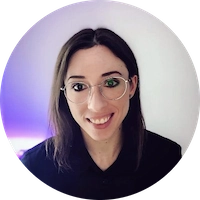 查理有着棕色的长发，戴着眼镜。她站在一面装有紫色灯光的白墙前。